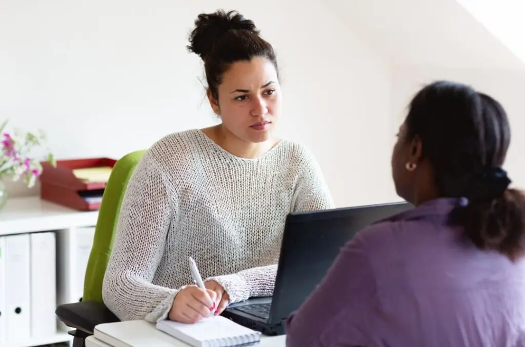 Community health worker talks with a client at their desk.