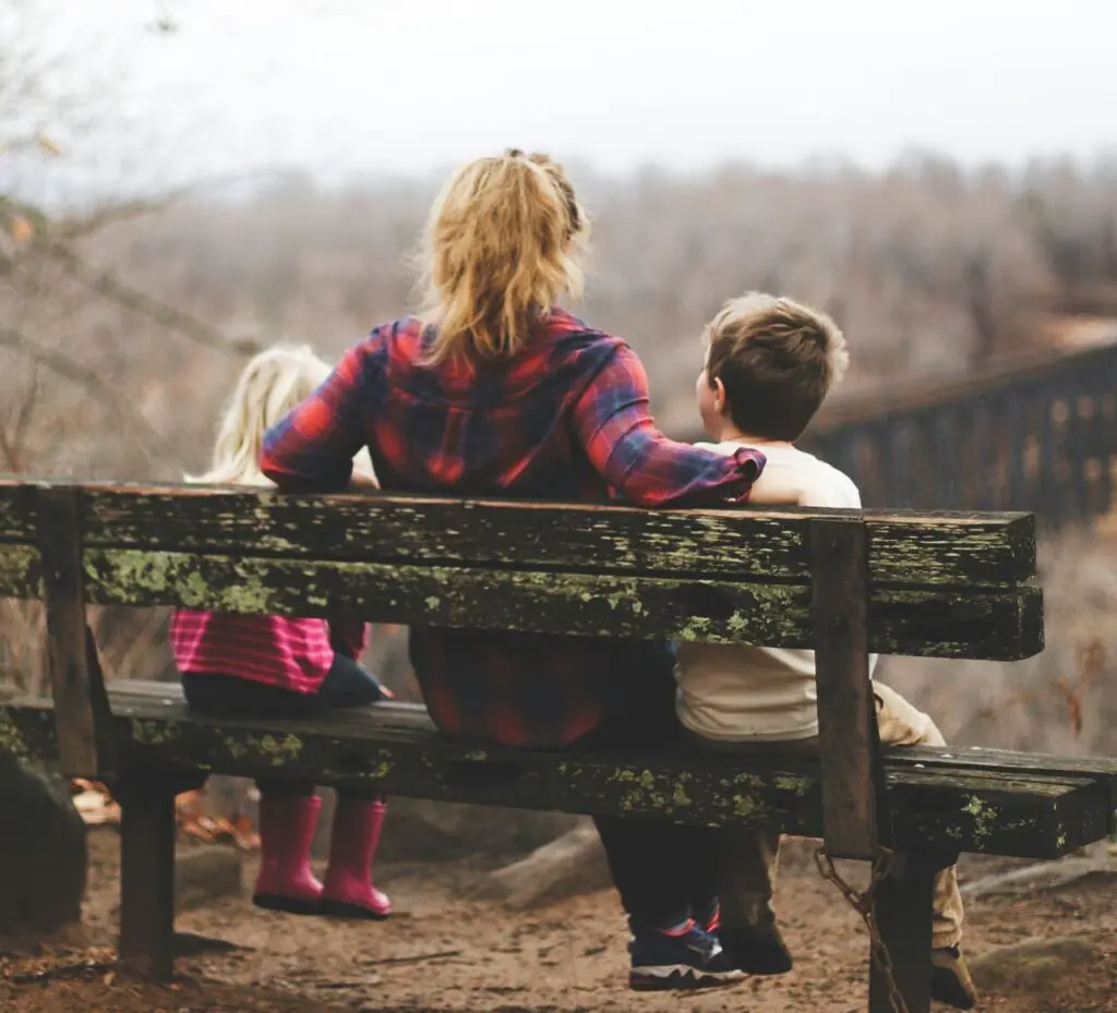 woman sitting with two children on a bench looking away